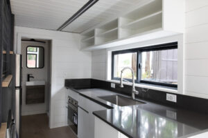 interior image of tiny house kitchen with quartz counters, lvp flooring, lap siding, and white kitchen cabinets