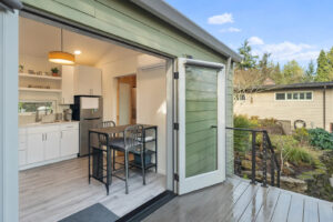 image of backyard cottage with green siding and glass french doors open to a kitchen with tng walls, white cabinets, and stainless appliances.
