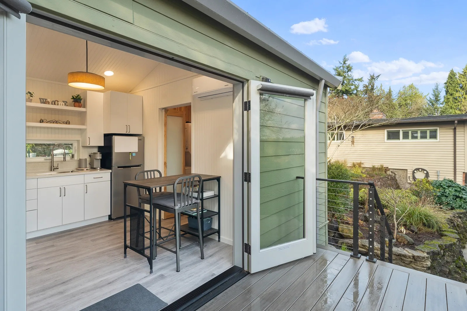 image of backyard cottage with green siding and glass french doors open to a kitchen with tng walls, white cabinets, and stainless appliances.