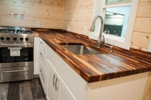 interior image of tiny house kitchen with butcher block counters, white cabinetry and a stainless range with oven