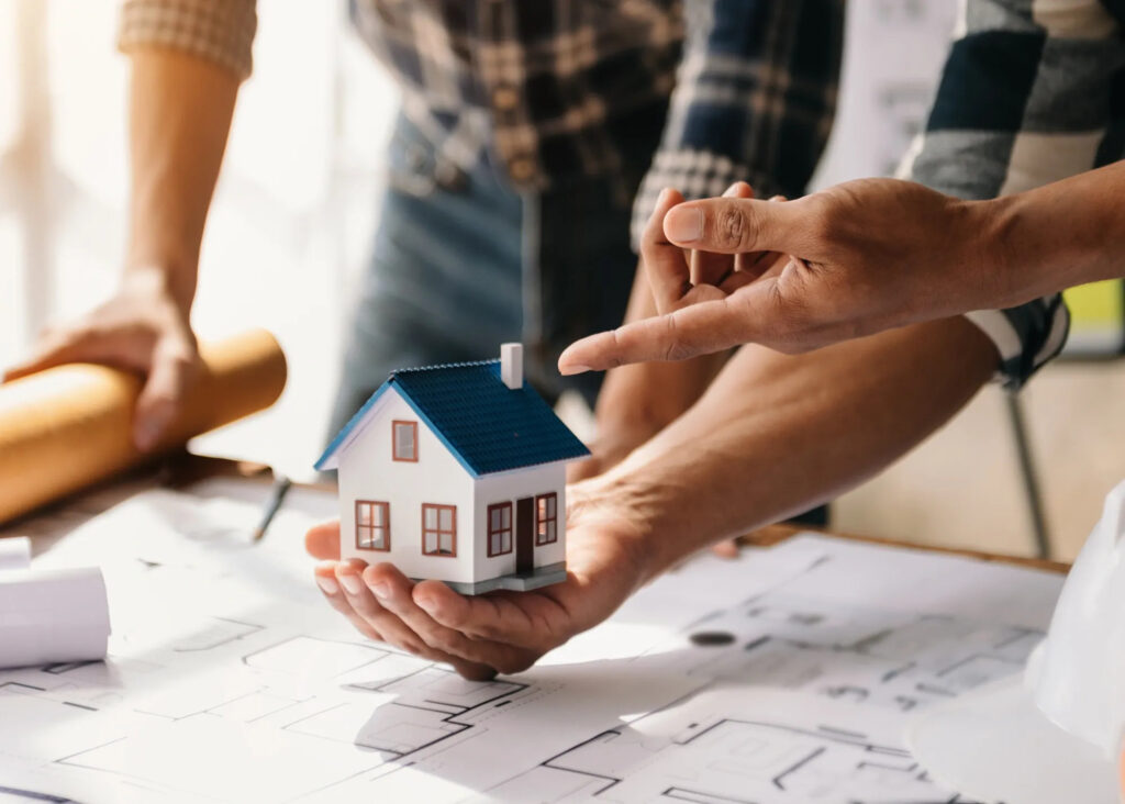 image of tiny house in a person's hand with architectural plans on the tabletop