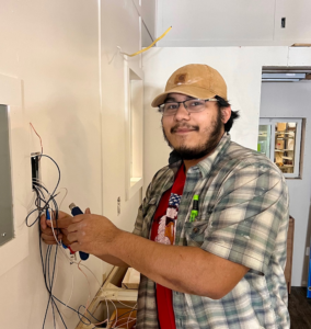 image of male in yellow cap and plaid shirt working on residential electric unit.
